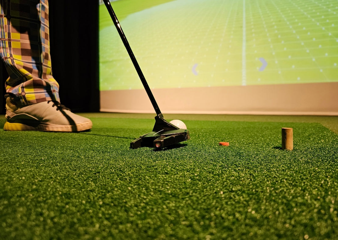 Person playing mini golf on a green surface with a digital screen in the background