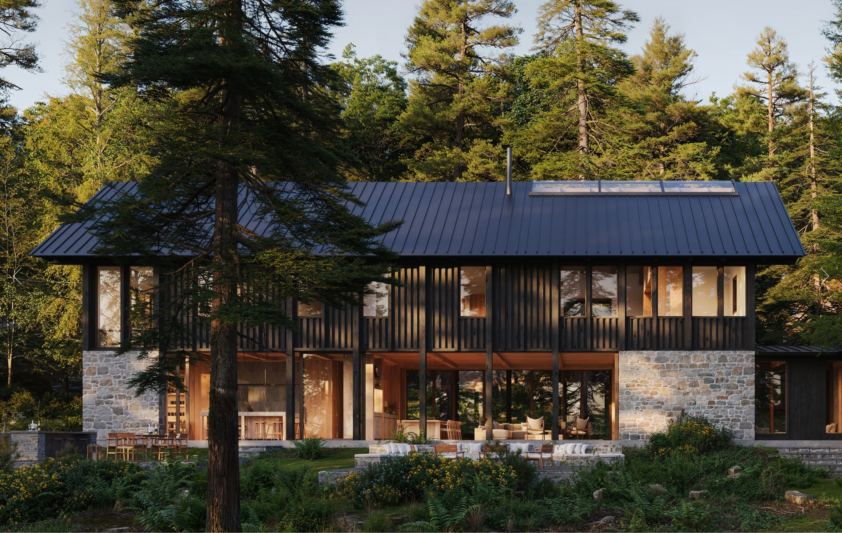 Modern cabin in the woods with a dark roof and stone foundation.