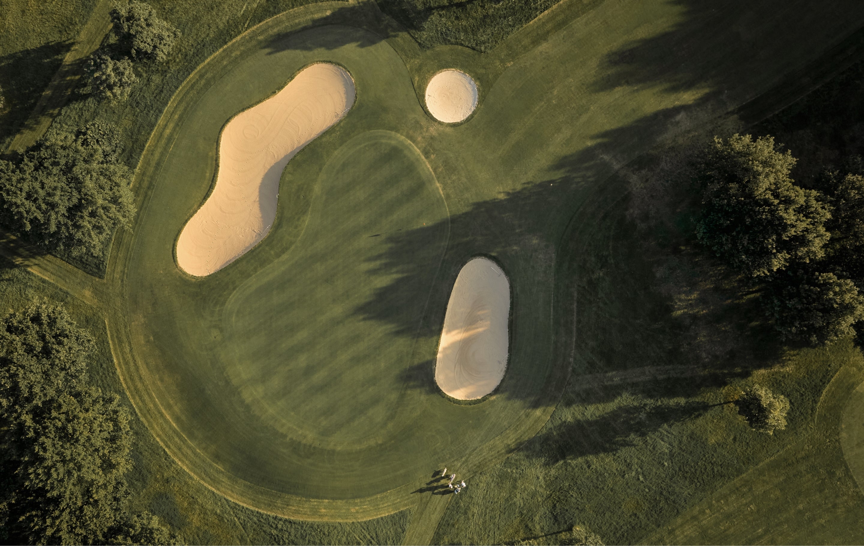 Golf course with sand bunkers and green grass, surrounded by trees.