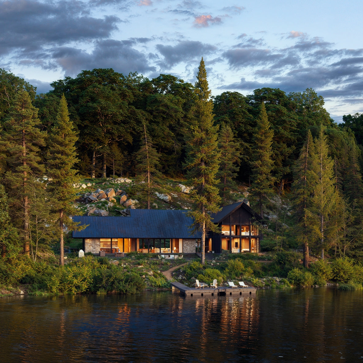Cabin in the woods by a lake with a dock at sunset.