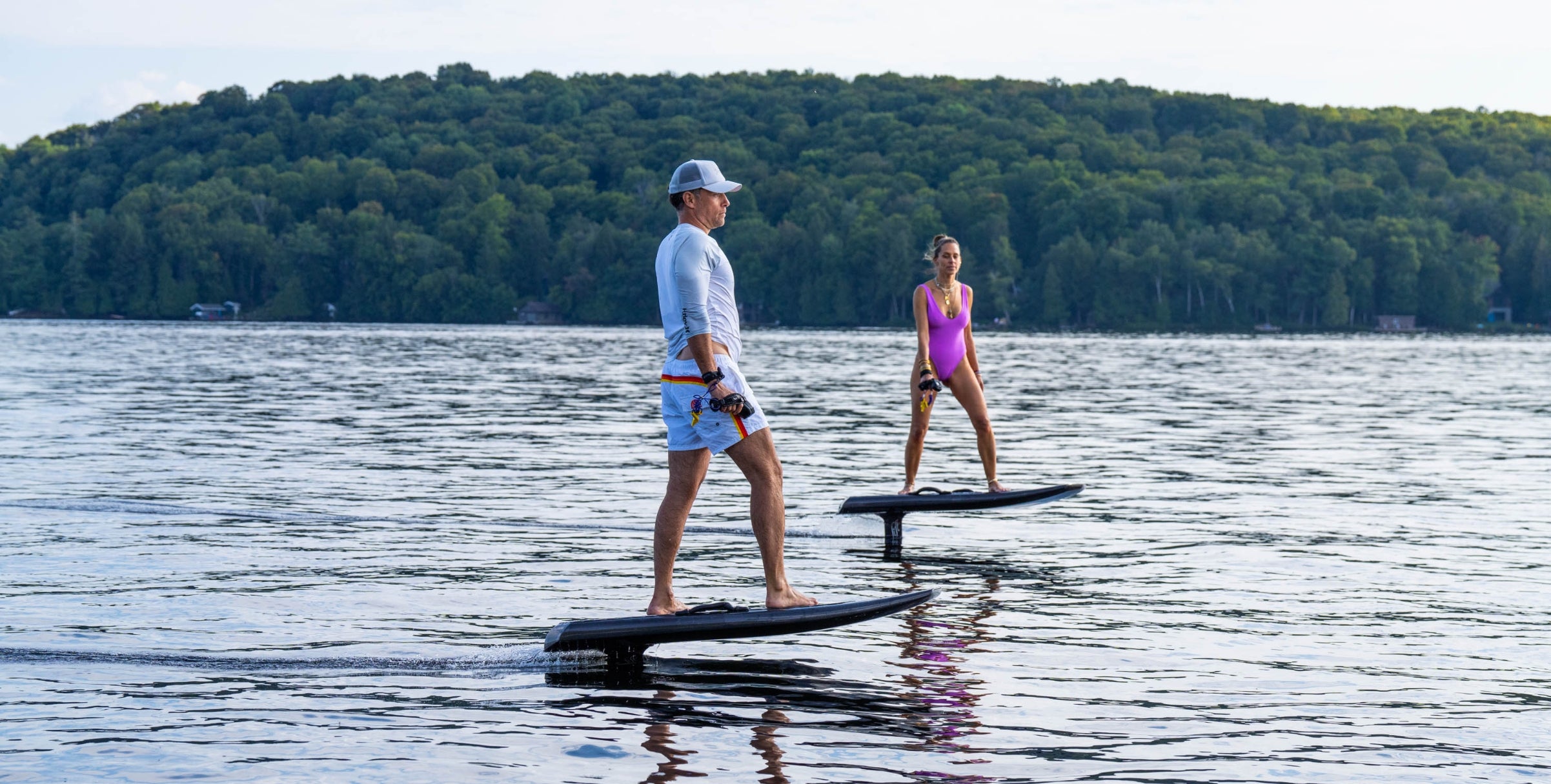 Two people on paddleboards on a lake with a forested shoreline.