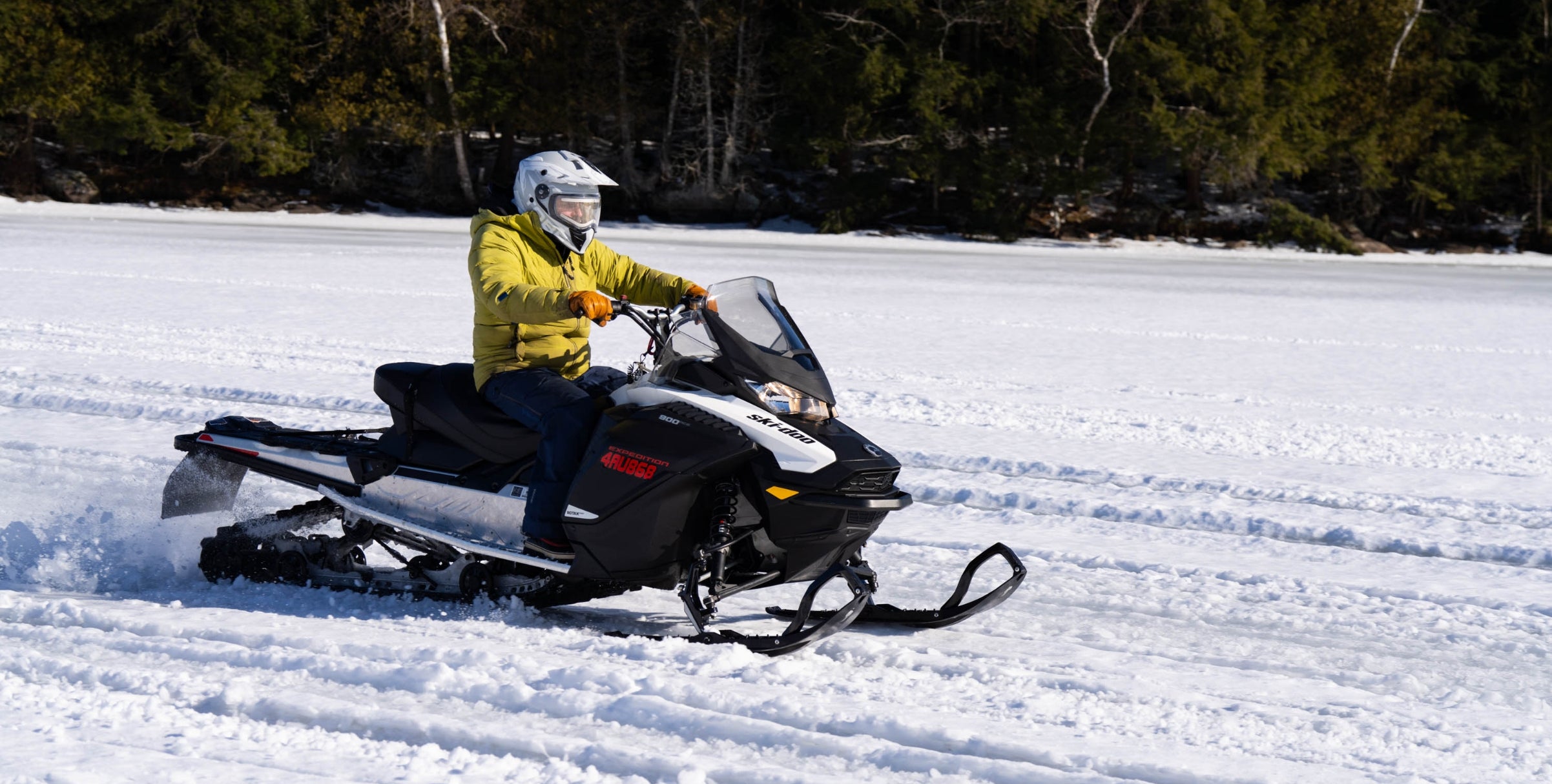 Person riding a snowmobile on a snowy landscape with trees in the background