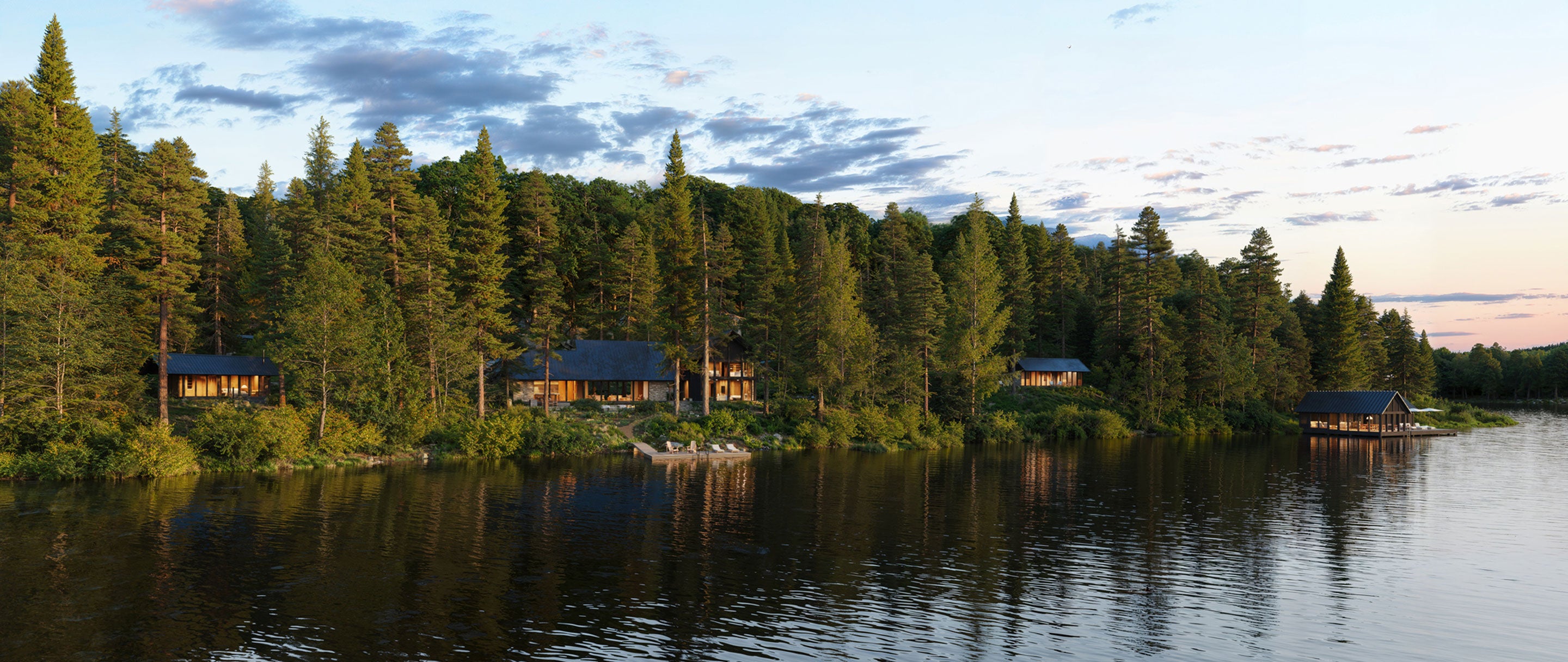 Scenic view of cabins nestled among trees by a lake with a sunset sky.