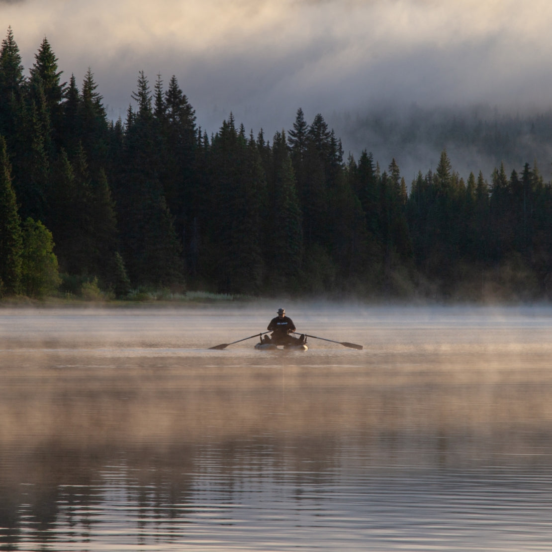 Person rowing a boat on a misty lake with trees in the background